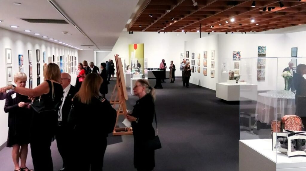 A group of people gather around and chat in an art exhibition area during a previous ArtsThrive event.