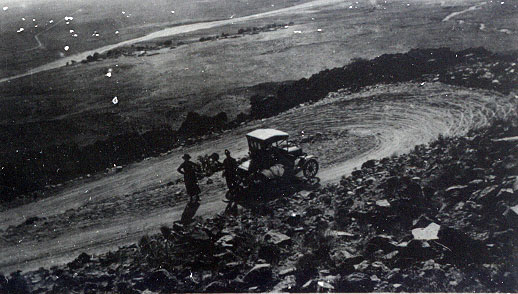 A vintage black and white photo of an old car on a dirt road.