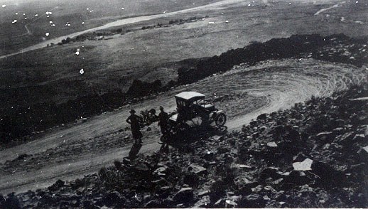 A vintage black and white photo of an old car on a dirt road.