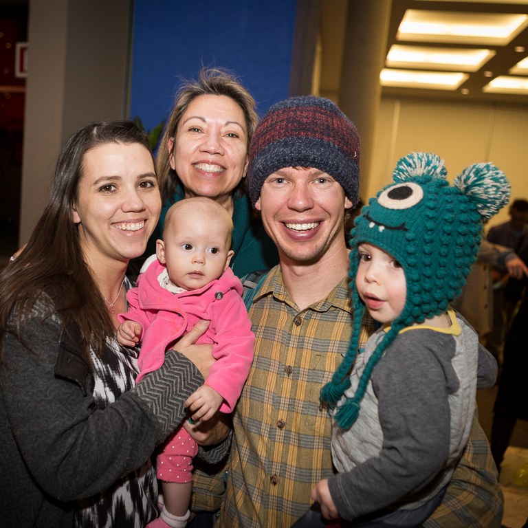 A group of people and children gather and pose for a photo, smiling at the audience.