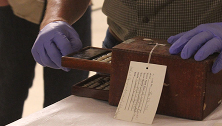 A photo of a collection piece being examined by the gloved hands of a museum staff member.