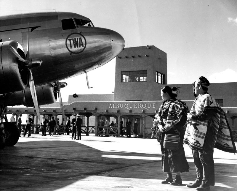 A woman and man stand on the tarmac outside the Albuquerque Airport looking at the nose of an airplane.