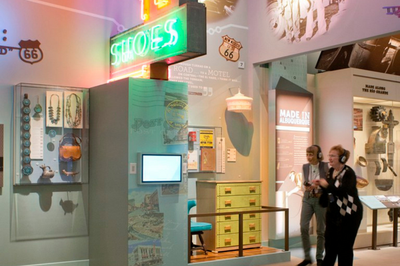 Two women standing in front of an art exhibit with neon lights, a dresser and a monitor on the wall.