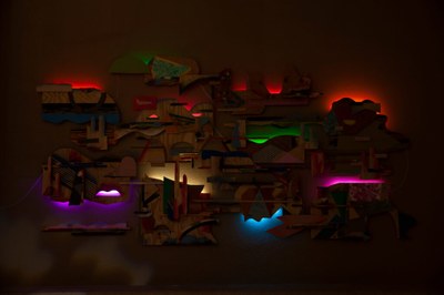 Karl Hofmann, Shapeshifters (detail) A picture taken of night of a wall-mounted work composed of organic-shaped pieces of work, illuminated from behind by colorful LEDs.