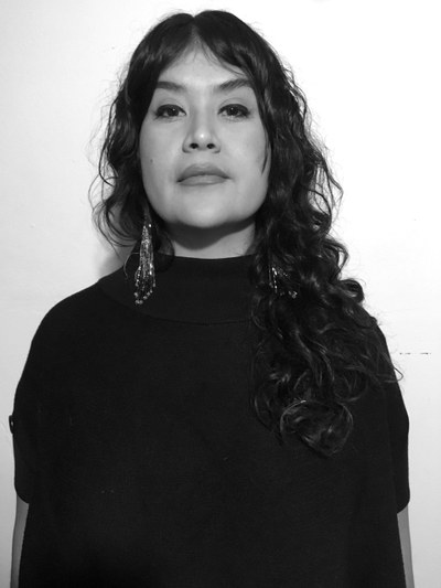 Nanibah Chacon Headshot A black-and-white headshot of artist Nanibah Chacon, who has long, wavy, dark-colored hair and wears large earrings and a black shirt.