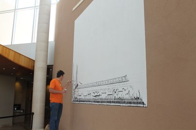 An image of artist Larry Bob Phillips working on his mural Eye Dazzler. He is painting in black over a white background.