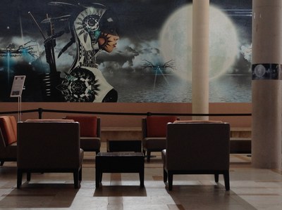 A large-scale image of a figure wearing futuristic armor and a quiver full of arrows against a background with a large moon, installed on a wall in the Albuquerque Museum lobby.