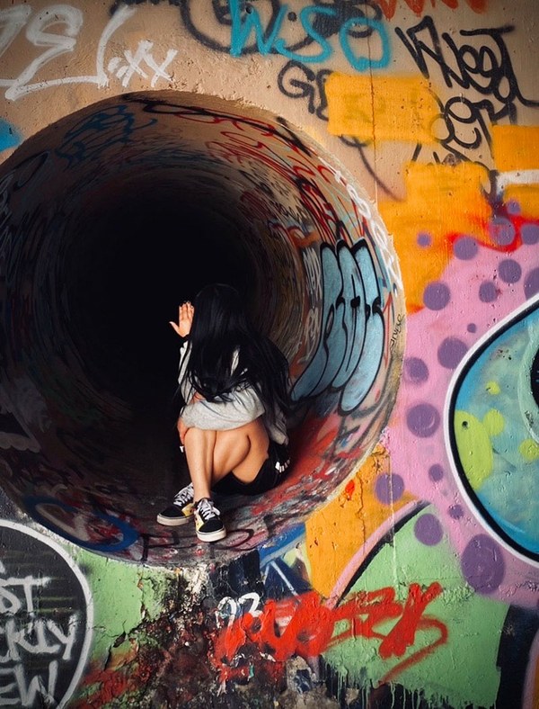 Young person couched in tunnel covered in graffiti