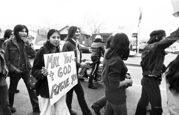 Anthony Louderbough, Demonstrator Holds Sign Reading, “May Your God Forgive You” Seven Generations 2020