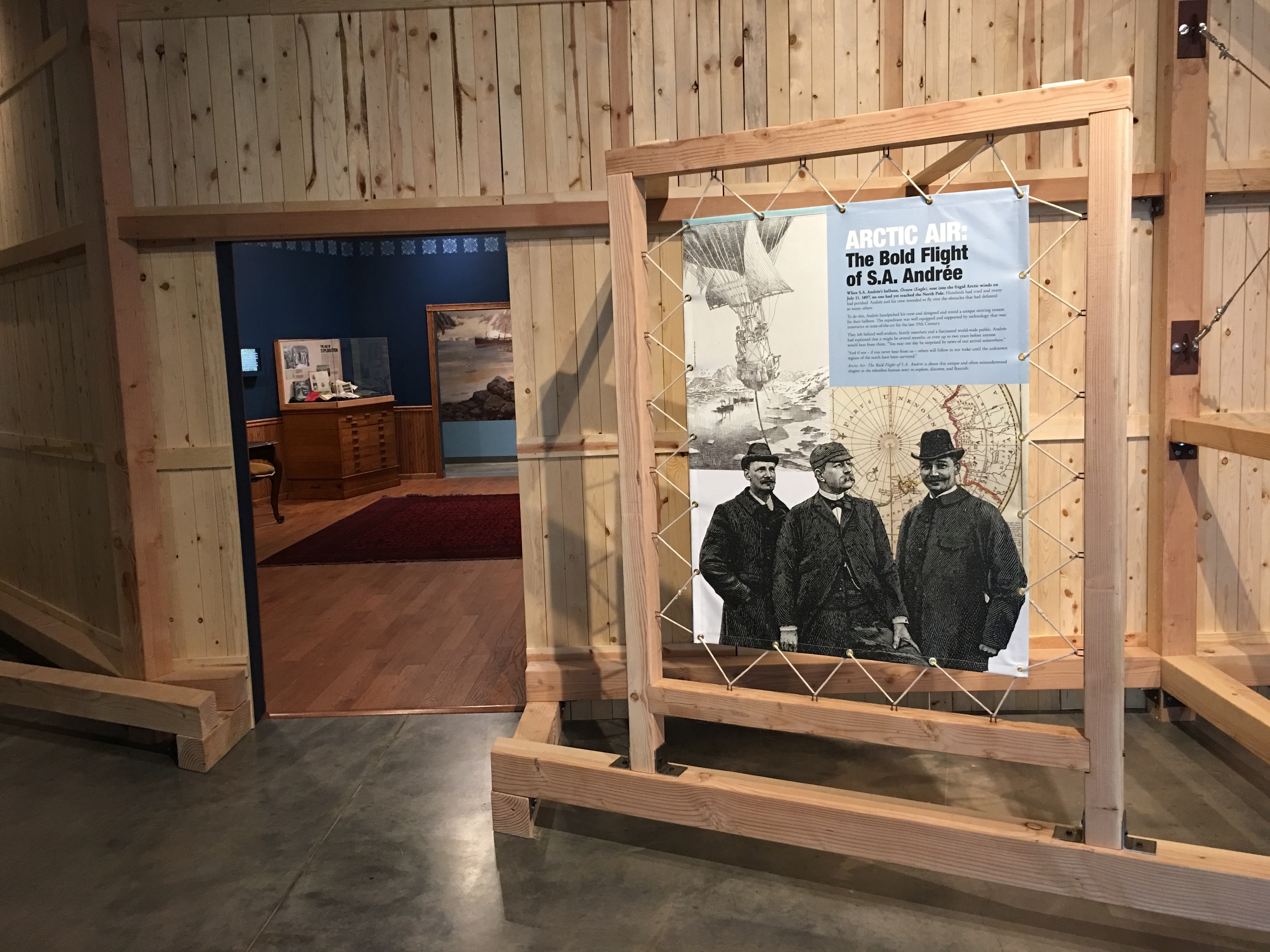 The Arctic Air Entry portion of the exhibition featuring a roomed lined with wood wall panels and a large photo of three men, part of the arctic expedition.