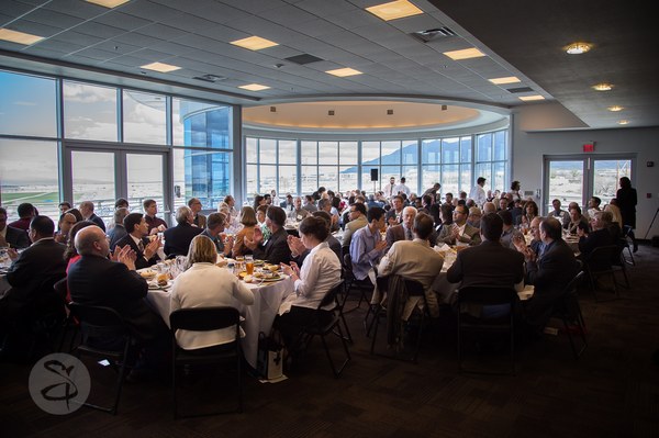 Balloon Museum Upstairs Event A room full of people in professional attire sitting at tables. The far wall in the room is all windows with a view of the mountains and Balloon Fiesta Park.