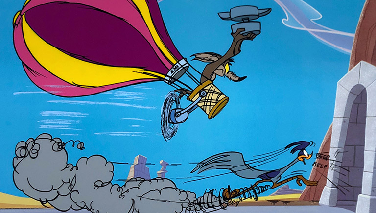 A close crop of a Loony Tunes artwork featuring the Roadrunner and Wile E. Coyote. Coyote is in a hot air balloon holding an anvil while perusing the road runner who is about to head into a tunnel.