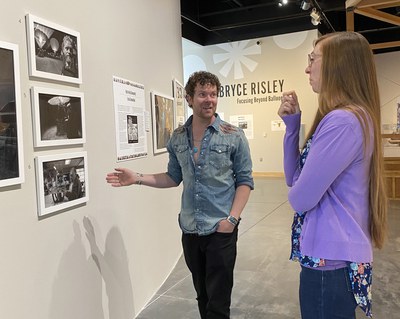 Bryce Risley converses with a woman and gestures to one of his photography pieces in the exhibition.