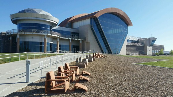 The rear exterior of the Balloon Museum featuring the large glass window and a seating area along the walkway.