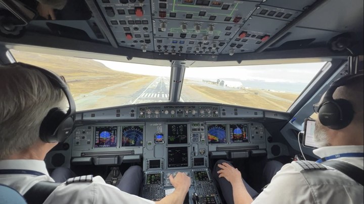 Two men inside the cockpit of a plane, looking out over the run way.