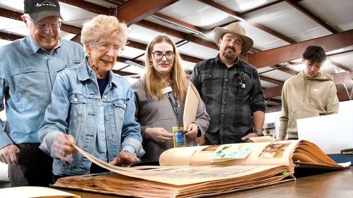 Family of balloonist Dewey Reinhard looks through scrap book with the Balloon Museum's Collections team.