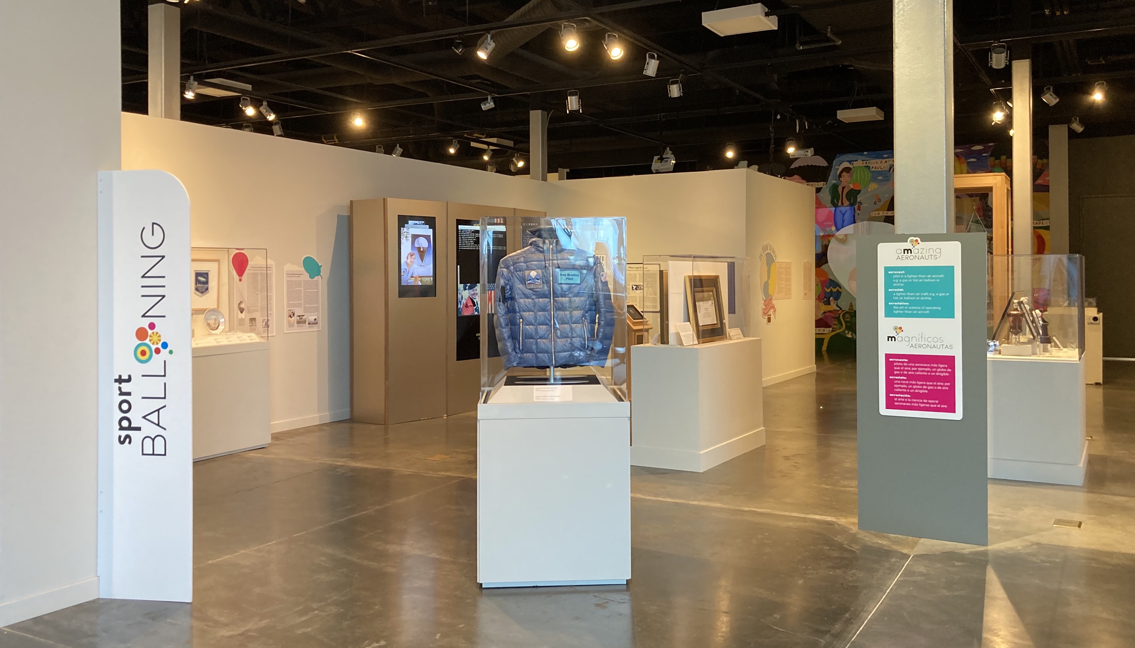 A view of several exhibits within the Sport Ballooning exhibition, including a jacket, various artworks under glass, and several informational displays.