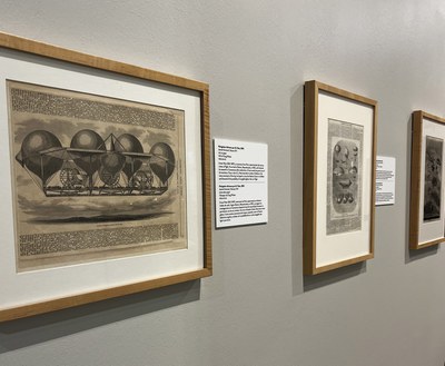 Three 2-D artworks, part of the Dirigible Dreams exhibition, all framed in a simple, light wood tone frame. All feature black ink newspaper illustrations from the mid 19th century with text copy artfully arranged around the illustrations.