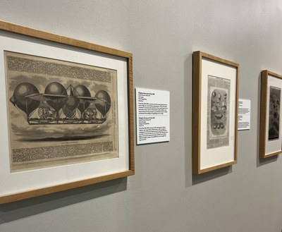 Dirigible Dreams Artworks Three 2-D artworks, part of the Dirigible Dreams exhibition, all framed in a simple, light wood tone frame. All feature black ink newspaper illustrations from the mid 19th century with text copy artfully arranged around the illustrations.