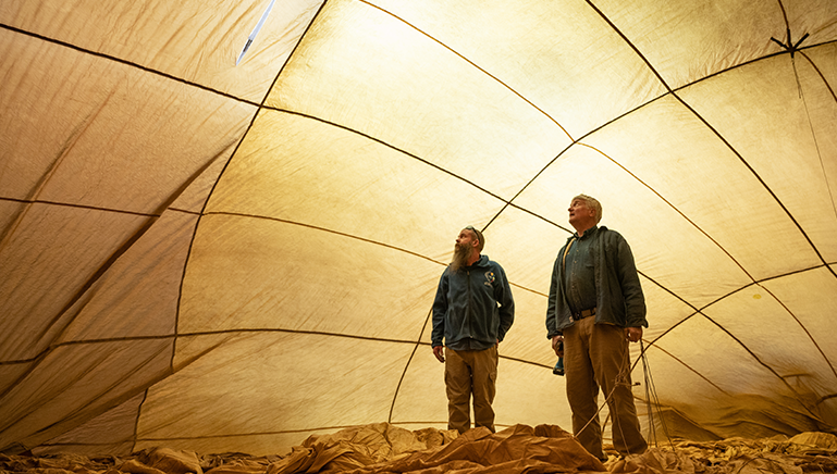 Two men stand inside an inflated hot air balloon.