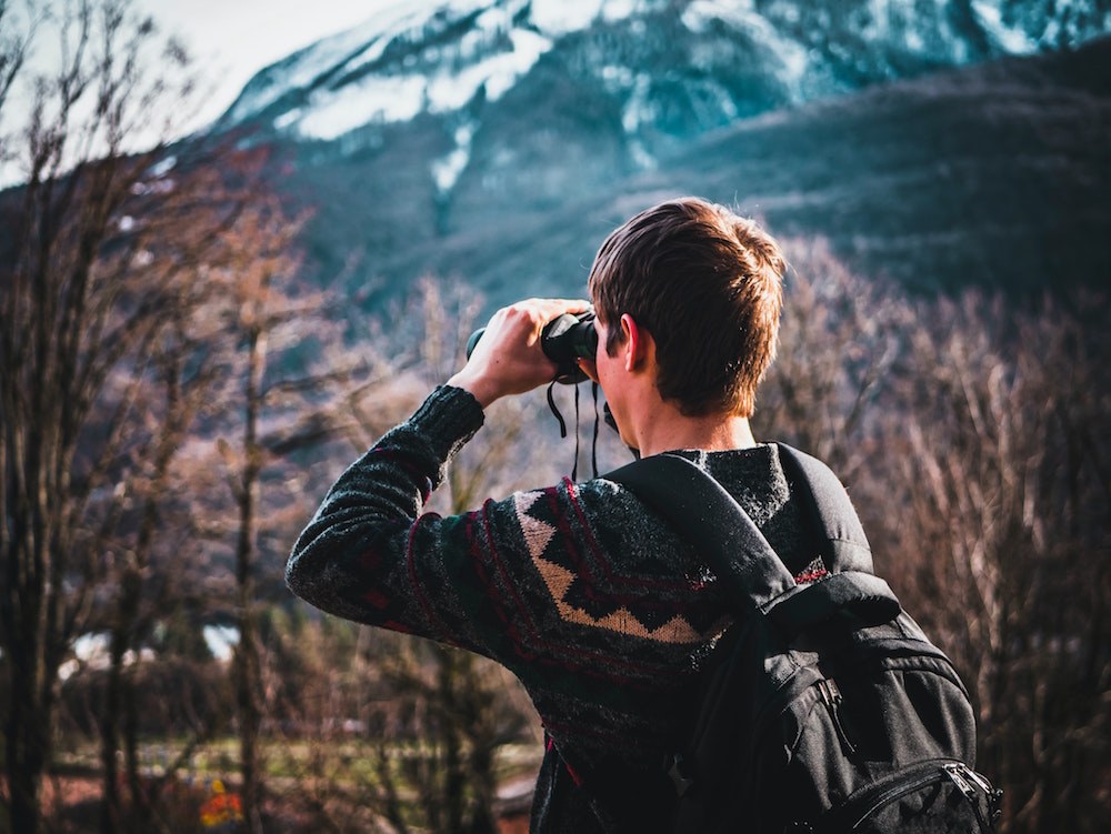 A person looks off in the distance with binoculars.