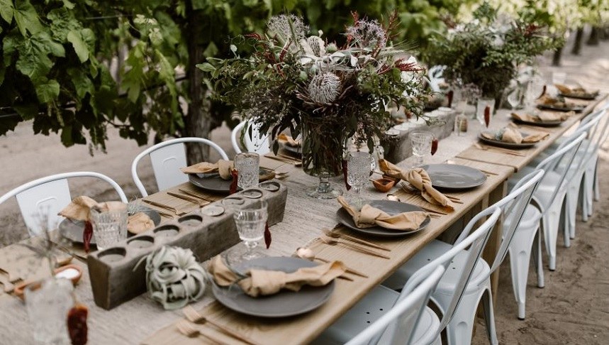 Event Booking Section Block Tile A decorated and set long table with lush greenery in the background.