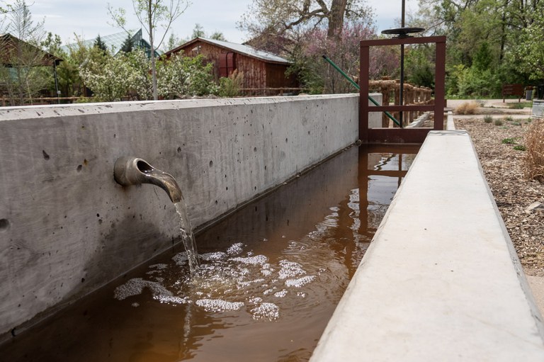 Water flows through a concrete acequia at Heritage Farm.