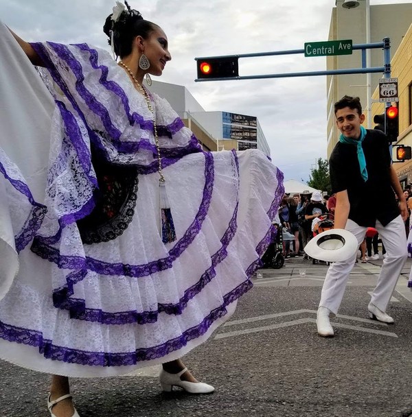 Dancers performing traditional Mexican folkloric dance on a city street under a Central Ave sign.