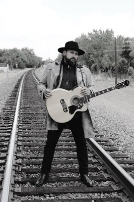 Black and white photo of man standing on train tracks, holding a guitar.