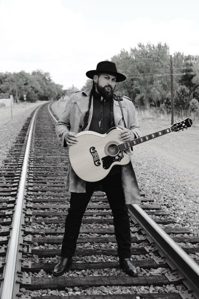Black and white photo of man standing on train tracks, holding a guitar.