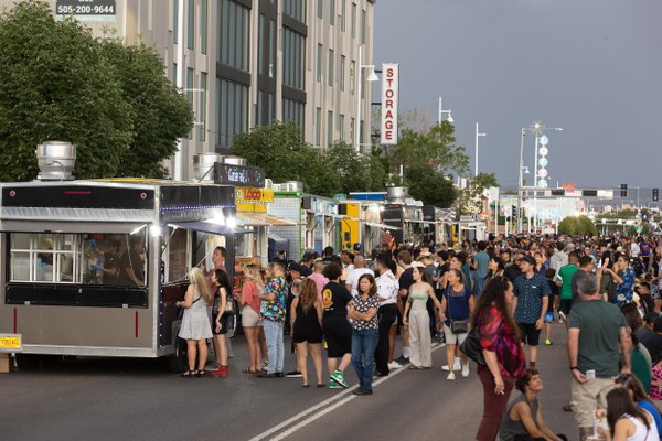 Crowd gathered along a city street lined with multiple food trucks under a cloudy sky.