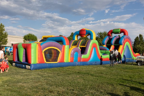 Colorful inflatable obstacle course set up on a grassy field with children and adults nearby on a sunny day.