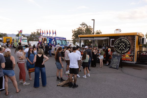 People waiting in line at various colorful food trucks during an outdoor event on a clear day.