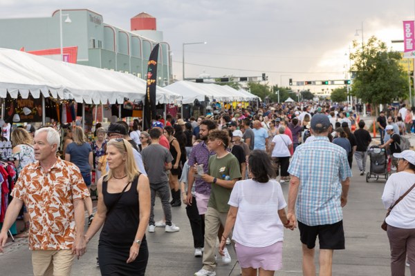 Crowds of people walk and browse vendor tents at an outdoor street market during daytime.
