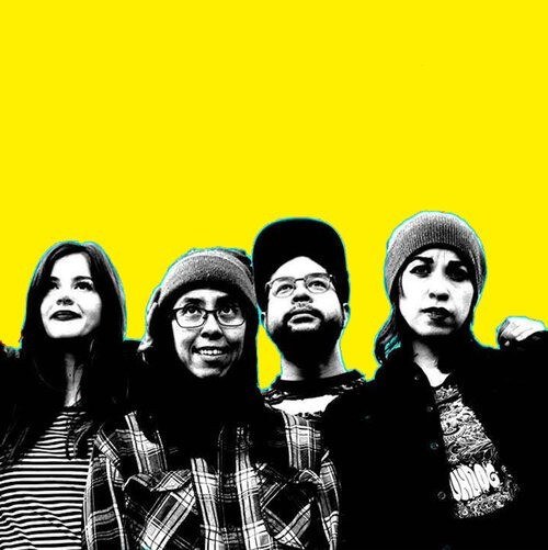 Prisim B Four young adults stand closely together against a bright yellow background, each with distinct casual styles and expressions.
