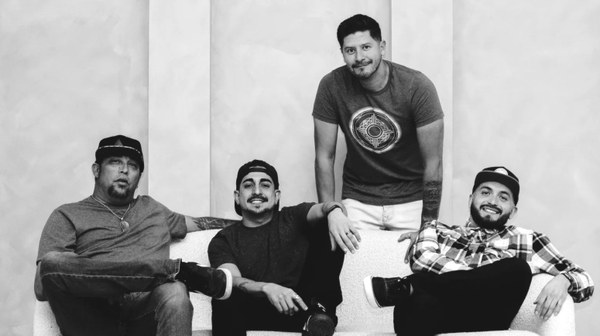 Vibe Strong Four men posing casually in a modern indoor setting, three seated on a white couch and one standing behind it, all smiling or relaxed.