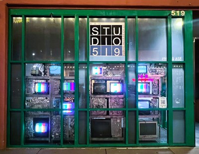 Art installation with multiple, stacked television screens lit up in a dark room.