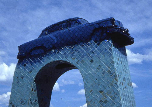 A large-scale, blue ceramic tile monument of a 1954 Chevy atop a large arched pedestal.