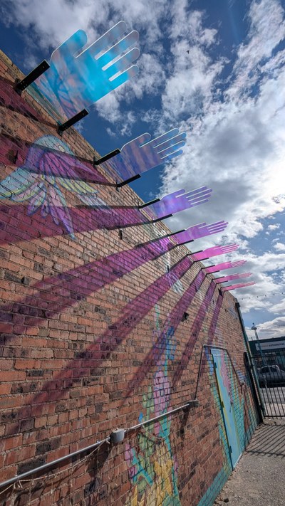Multi-colored, acrylic hands installed on the side of a brick building.