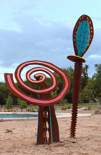 Part of a series of seven free standing rusted steel sculpture towers with various whimsical objects at the top which are painted in bright vivid colors.