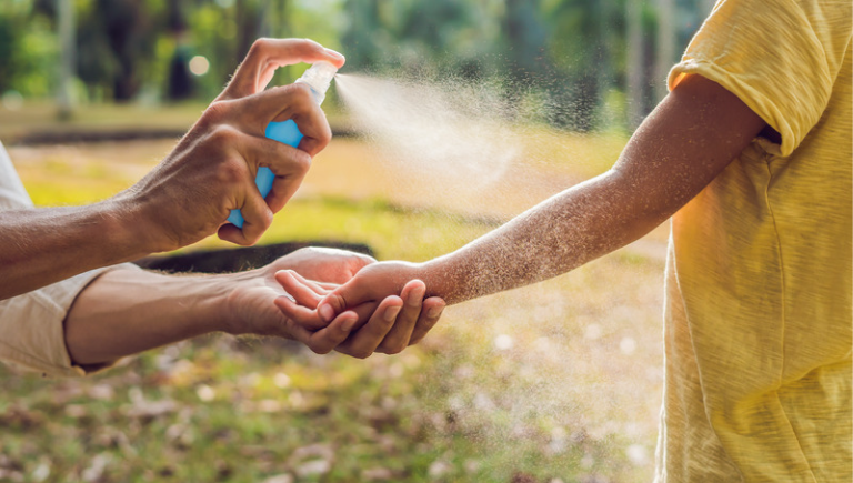 An adult spraying bug spray on a childs arm.