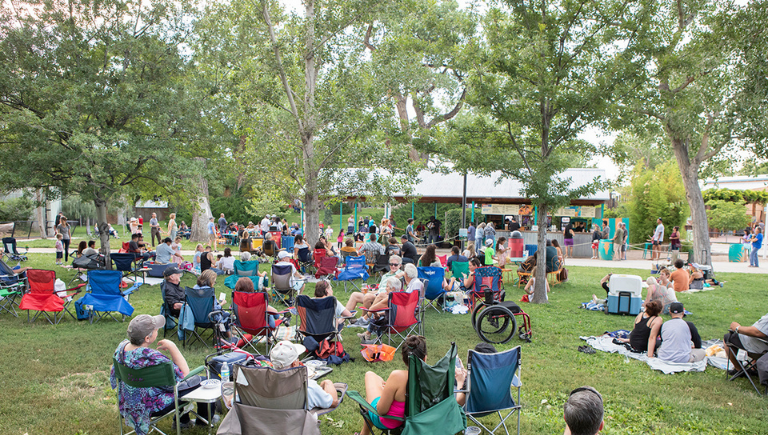 Dozens of people on chairs in grass in front of the Botanic Garden amphitheater.