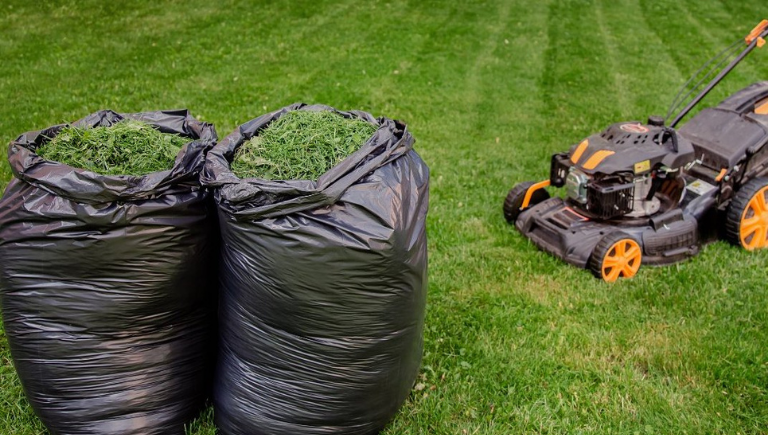 A PNG of two black trash bags filled with grass clippings next to an orange lawn mower.
