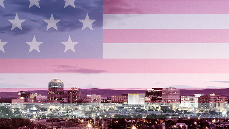A sunset view of downtown Albuquerque's skyline with a faded overlay of the flag of the United States of America.