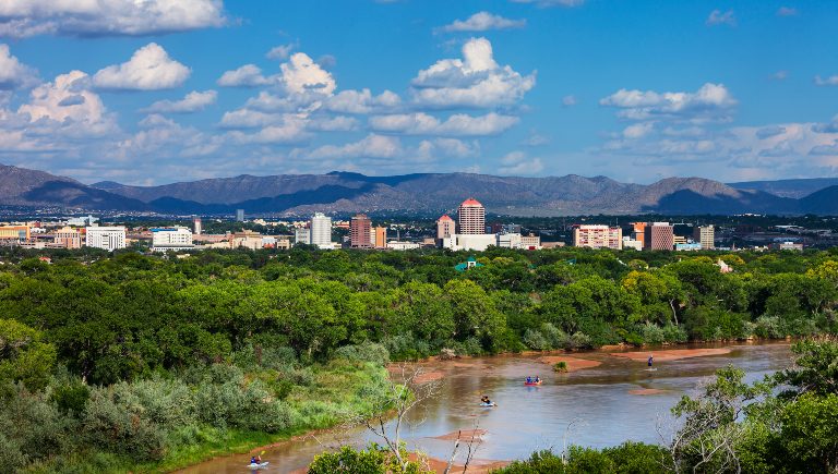 Kayakers paddling on the Rio Grande River with Downtown Albuquerque and the Sandia Mountains in the foreground.