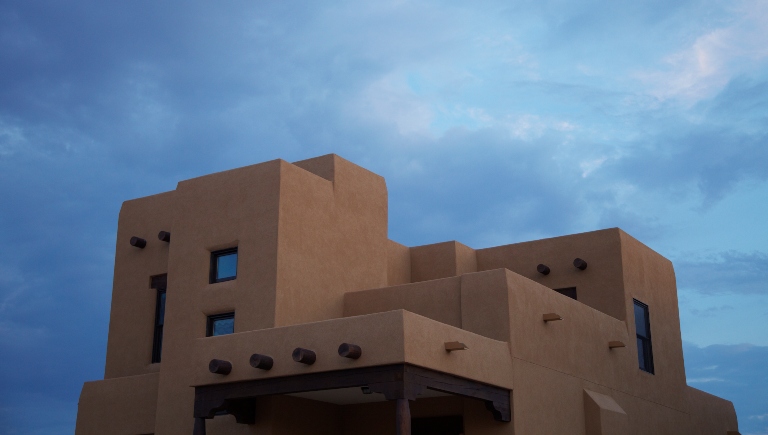 A multi-story light beige stucco building with a blue, partially cloudy sky in the background.