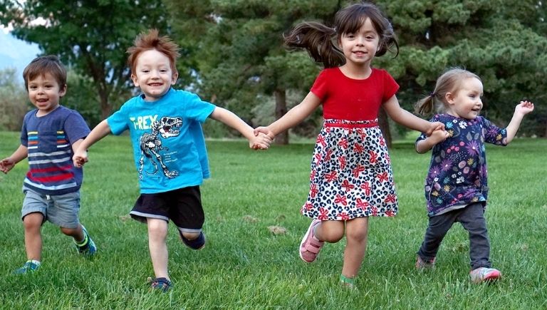 Four children running in a park while holding hands.