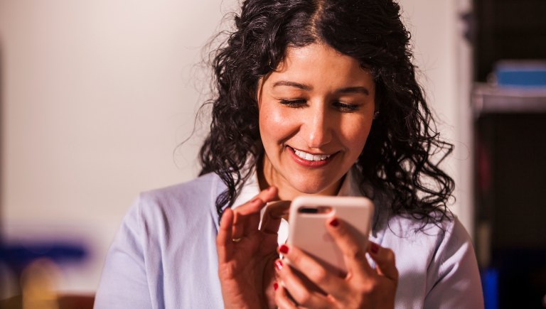 A woman smiling as she types on her phone.