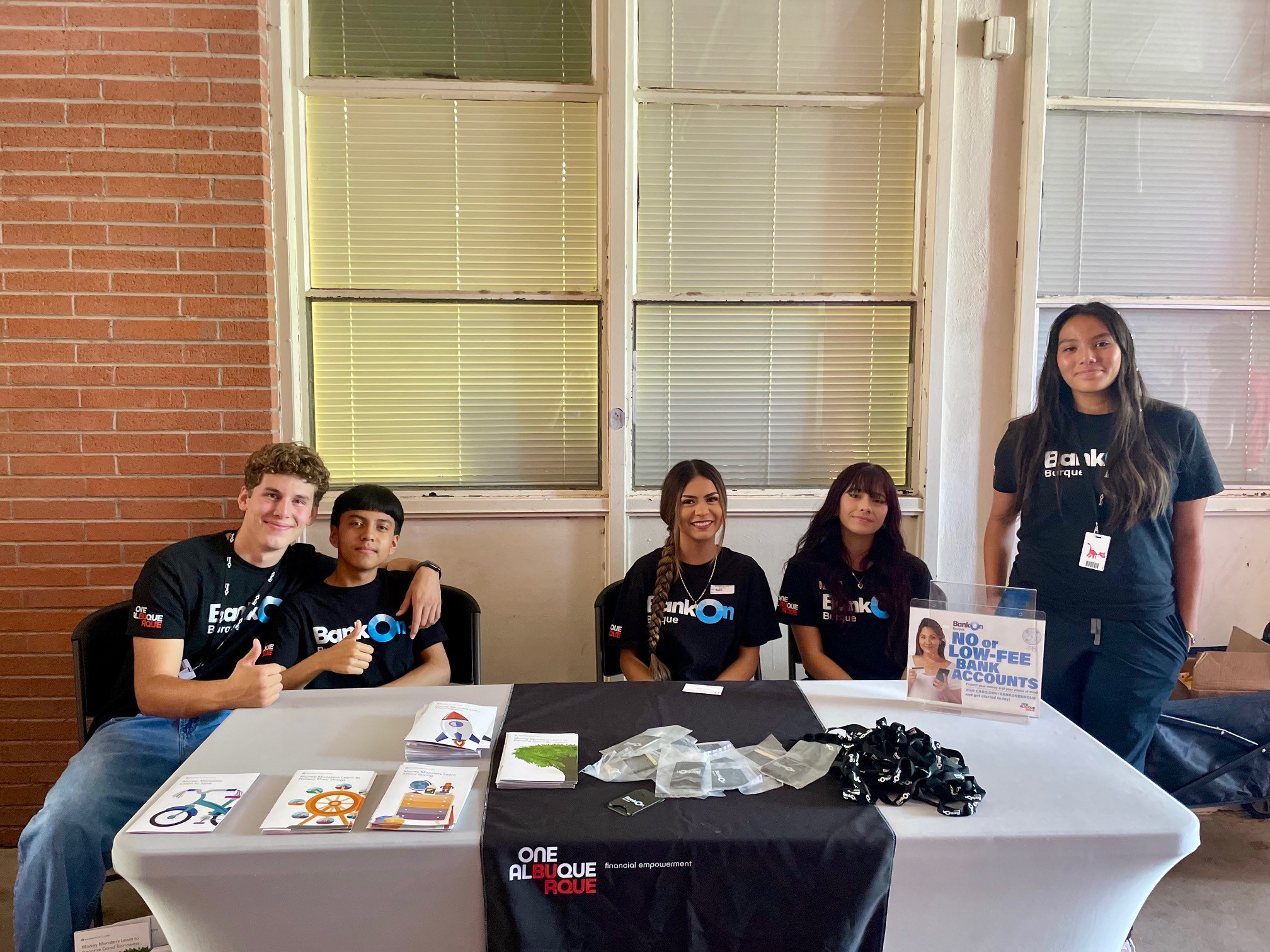 Group of young men and women sitting in front of a table that has Bank On resources.