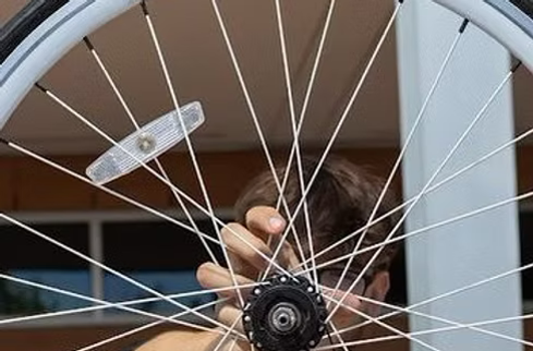 A teen holds a bicycle wheel up in front of the audience.
